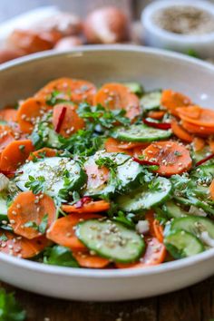 a white bowl filled with cucumbers and carrots on top of a wooden table