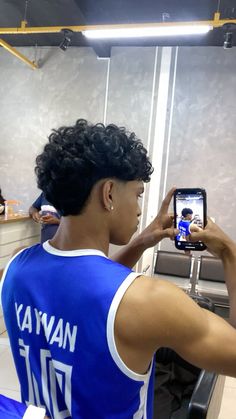 a young man taking a selfie with his cell phone in front of him while wearing a blue jersey