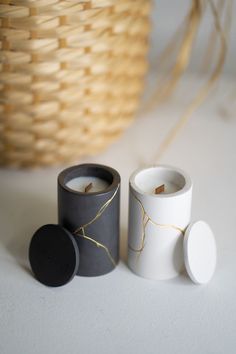 two candles sitting next to each other on a white surface with a basket in the background