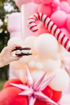 a person holding a piece of cake in front of some balloons and candy canes