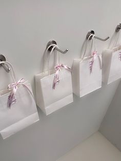 three white bags hanging on the wall with pink ribbons tied around them and two silver spoons sticking out of each bag