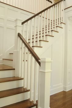 a white staircase with wooden handrails and wood flooring in a home's entryway