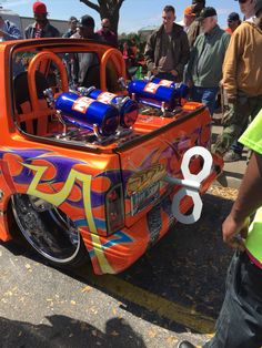 an orange truck with some blue cans in the bed and people standing around looking at it