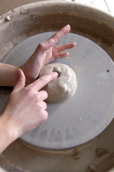 two hands reaching for something in the middle of a bowl that is filled with clay