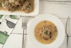 a white plate topped with meat and gravy next to a bowl of soup