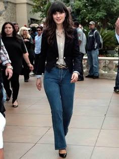 a woman walking down the street wearing jeans and a blazer with gold buckles