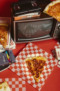 two slices of pepperoni pizza on red checkered paper next to an old tv