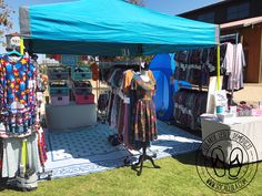 an outdoor market with clothing on display under a blue tent