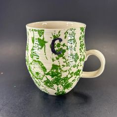 a green and white coffee cup sitting on top of a table next to a black surface