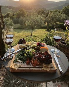 two glasses of wine are sitting on a table with cheese and fruit in the foreground