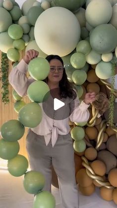 a woman standing in front of a bunch of balloons with green and white balls hanging from the ceiling