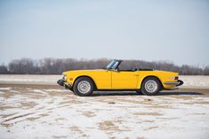 an old yellow sports car parked in the middle of a snowy field on a sunny day