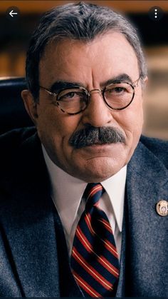 an older man with glasses and a mustache wearing a suit jacket, tie and eyeglasses