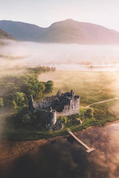 an aerial view of a castle surrounded by fog and low lying hills in the distance