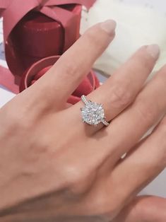 a woman's hand with a diamond ring on it and a pink ribbon in the background