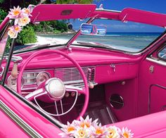 a pink car parked on the beach with flowers in the dash board and steering wheel