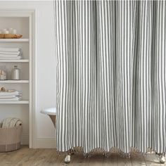 a bathroom with a striped shower curtain next to a bathtub and shelves filled with towels