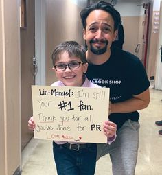 a man holding a sign next to a little boy with glasses and a mustache on his head