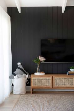 a living room with black walls and wicker furniture, large screen tv on the wall