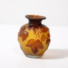 a yellow vase with leaves painted on the front and sides, sitting on a white surface