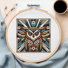 an owl cross - stitch pattern is shown on a table next to a cup of coffee