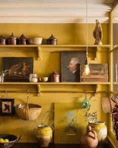 a room with yellow walls and shelves filled with vases, bowls and other items