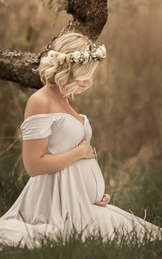 a pregnant woman sitting in the grass with her hands on her stomach wearing a flower crown