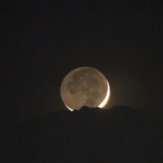 the full moon is seen in the dark sky above a mountain range at night time