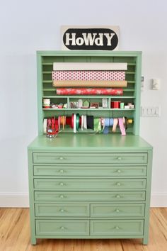 a green dresser with lots of crafting supplies on it's top and bottom shelf