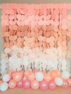 an arrangement of balloons and paper flowers are displayed on a table in front of a backdrop