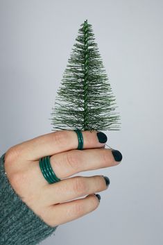 a woman's hand holding a small green christmas tree on top of her finger