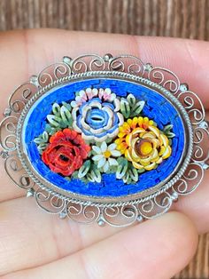 This is one of the prettiest micro mosaics I have come across with its bright colors and raised petal design. The flowers are two toned with golden orange, blue and red as the predominant colors and a little white daisy in the pattern. The blue border is bright and deep and the raised pieces really add depth and unique dimension to the brooch.  The setting is silver toned and the border has pretty see through filigree. The back is unmarked and the brooch measures 1 1/2 inches long. Multicolor Cabochon Brooch As Gift, Multicolor Cabochon Brooch For Gift, Multicolor Cabochon Brooches As Gift, Multicolor Cabochon Brooches For Gifts, Multicolor Cabochon Brooches For Collectors, Antique Multicolor Brooch For Gifts, Antique Multicolor Brooches As Gifts, Unique Multicolor Cabochon Brooches, Handmade Multicolor Flower Brooch