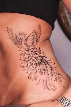 a woman's stomach with a bird and flowers tattoo on her side ribcage