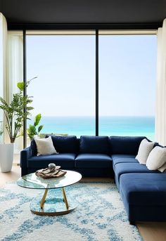 Create a luxurious coastal-inspired living room, featuring light and airy blues, whites, and neutrals. The space should have a modern, open-plan design with floor-to-ceiling windows that offer panoramic ocean views. Include a large, plush sofa upholstered in soft navy blue, paired with white and light wood accents. Add a chic glass coffee table with a mirrored surface, and a textured blue-and-white rug beneath. Incorporate organic textures, such as a driftwood sculpture Blue And White Rug, Driftwood Sculpture, Organic Textures, Plush Sofa