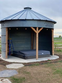 a large metal structure with a mattress in it's center surrounded by grass and dirt