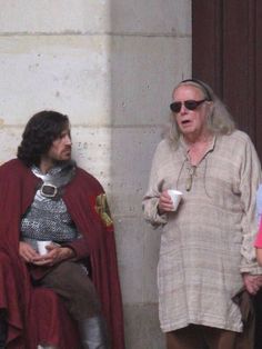 two men dressed in medieval clothing standing next to each other and one holding a cup