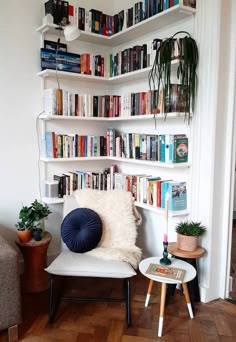 a white book shelf filled with books next to a small table and chair in front of it