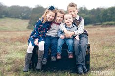 three young children sitting on top of an old pickup truck in a field with trees and grass behind them