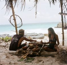 a man and woman sitting on the beach next to each other with food in front of them