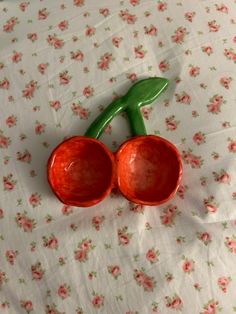 two red plastic cherries sitting on top of a flowered tablecloth with pink flowers