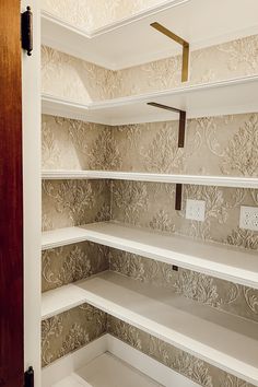 an empty pantry with white shelves and wallpaper