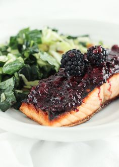 a white plate topped with meat and berries on top of greens next to a salad