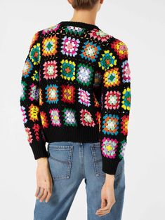 a woman wearing a black sweater with multicolored crocheted flowers on it