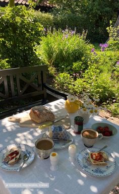 an outdoor table with food on it in the middle of some bushes and flowers,