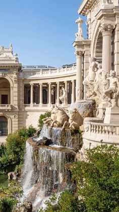 an ornate building with fountains and statues in the foreground, surrounded by greenery