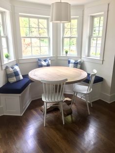 a table and chairs in a room with white walls, wood flooring and windows