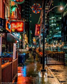 a city street at night with people walking on the sidewalk and buildings in the background