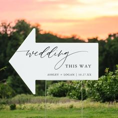 a wedding directional sign in front of the setting sun with trees and bushes behind it