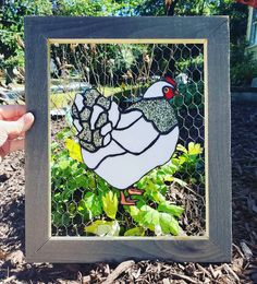 a hand holding up a chicken in front of a fenced in area with plants