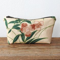 a small pouch with flowers on it sitting on top of a wooden table next to a white wall